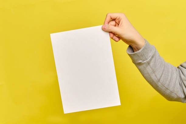 istock Copy space. Man hands holds a white paper sheet on a yellow background. 1216048042