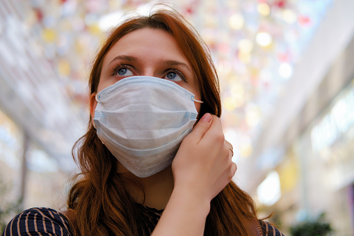 Una mujer joven está considerando si se debe quitar la máscara médica después del final de la cuarentena debido al coronavirus. Retrato de una niña después de la epidemia del virus de la gripe, de cerca photo