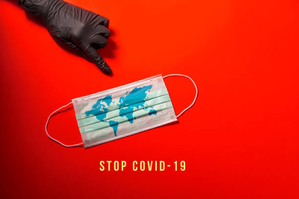 istock COVID-19, Hand in protective glove, points out surgical mask with world map. Red background. 1216055240