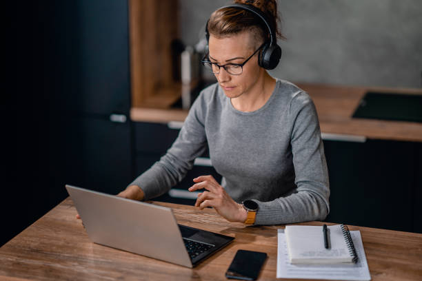 Woman wearing headphones and watching a webinar Focused woman wearing headphones, watching a webinar and writing notes. half shaved hairstyle stock pictures, royalty-free photos & images