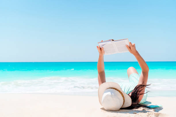 istock Young woman reading book during tropical white beach 1216057549