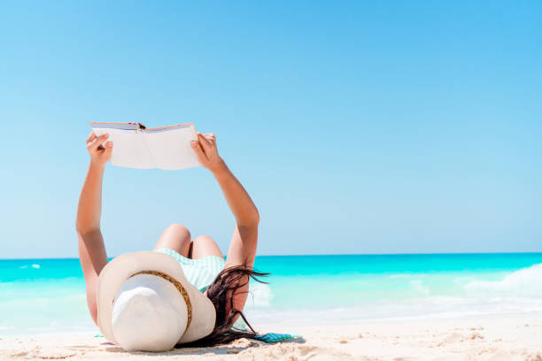 istock Young woman reading book during tropical white beach 1216057566