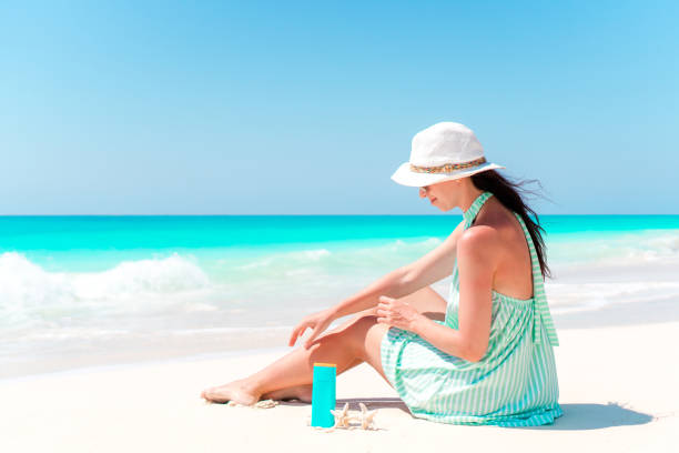 istock Beautiful young woman holding a suncream lying on beach 1216071966
