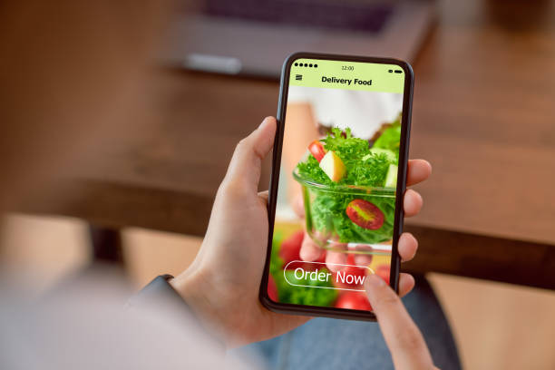istock Woman using smartphone and touching application screen for ordering salad online on table at the home. 1216073657