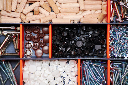 Dowels, screws, caps, and bolts sorted in the plastic container tools. Home repair equipment. Top view. Background texture
