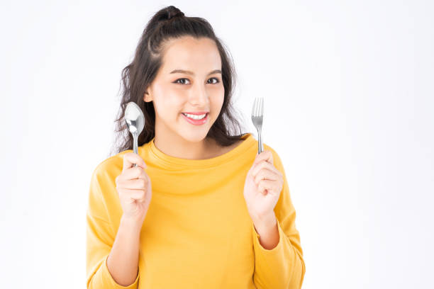 joven belleza asiática mujer mostrando cuchara y tenedor prepararse para comer comida y ella usando un suéter amarillo tiro aislado en fondo blanco - women spoon tasting elegance fotografías e imágenes de stock
