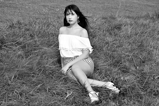 A black and white snapshot of a lovely young woman sitting on a grass field at a public park.