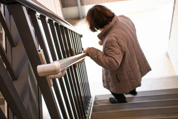 An elderly woman holding a railing and going down the stairs.