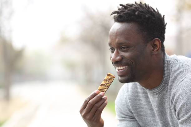 istock Happy black man eating a cereal bar in a park 1216086777