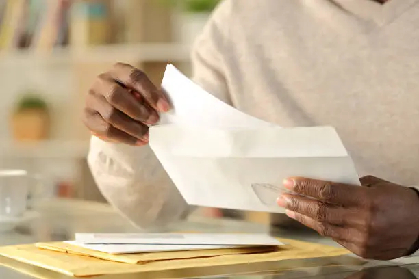 Close up of black man hands putting a letter inside an envelope on a desk at home