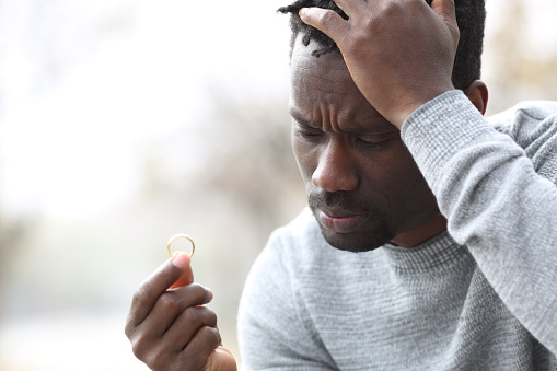 Sad black man complaining looking at wedding ring outdoors in a park