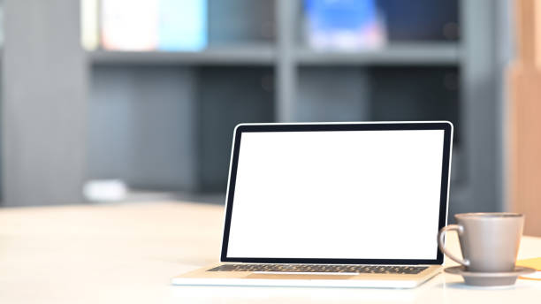istock Photo of Computer laptop with white blank screen putting on white working desk with coffee cup, clipboard over modern living room as background. Orderly/Comfortable workplace concept. 1216089759