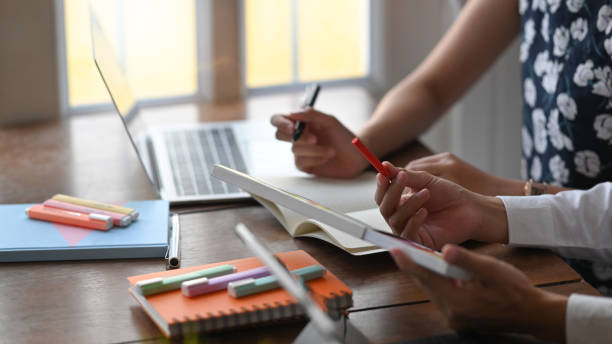istock Cropped image of graphic designer team talking/discussing/brainstorming about their project while selecting color and sitting together at wooden working desk over orderly living room as background. 1216090803