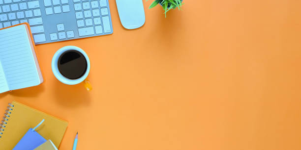 istock Top view image of colorful workspace. Wireless keyboard, mouse, coffee cup, notebook, diary, pencil and potted plant putting together on orange working desk. 1216090987