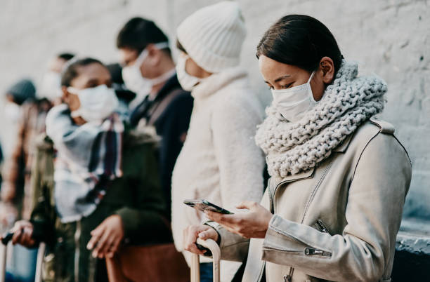 An informed community is a healthy one Shot of a young woman using a smartphone and wearing a mask while travelling in a foreign city covid crowd stock pictures, royalty-free photos & images