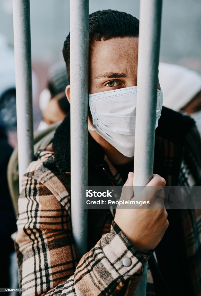 It wasn't me, it was corona Shot of a young man wearing a mask while stuck behind a gate in a foreign city Cage Stock Photo