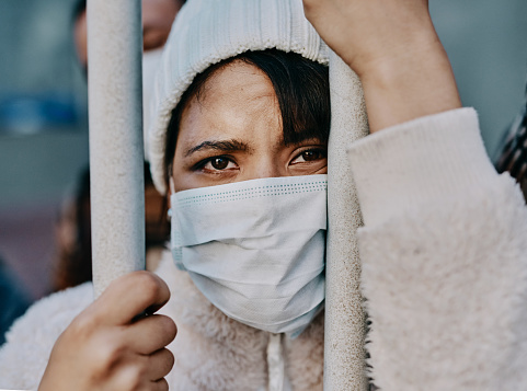 Shot of a young woman wearing a mask while stuck behind a gate in a foreign city