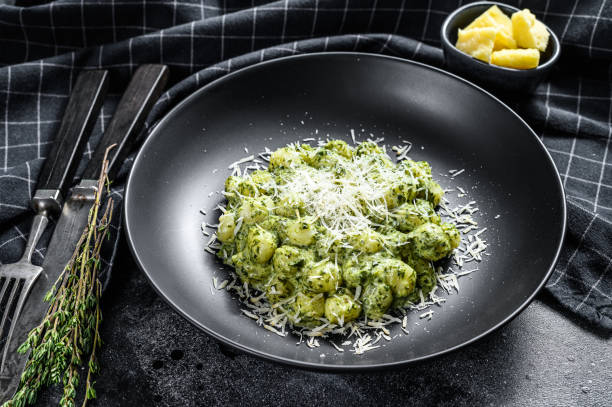 istock Gnocchi with basil spinach sauce and Parmesan. Italian potato paste. Black background. Top view 1216097560
