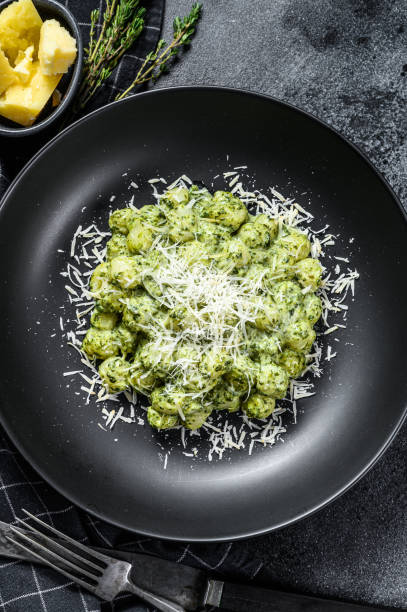 istock Gnocchi with basil spinach sauce and Parmesan. Italian potato paste. Black background. Top view 1216097772