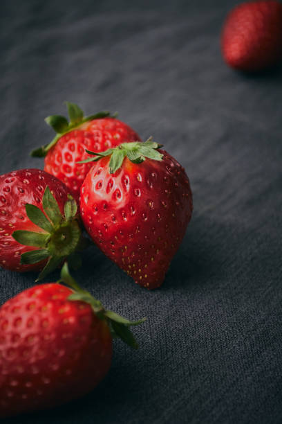 Close up of a fresh strawberries with leaves and selective focus. Close up of a fresh strawberries with leaves and selective focus, on a dark background. Healthy food lifestyle concept. vibrant color lifestyles vertical close up stock pictures, royalty-free photos & images