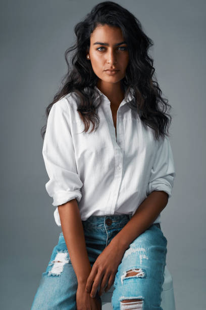 Denim and a white blouse, always a classic Studio shot of a beautiful young woman posing against a grey background blouse stock pictures, royalty-free photos & images