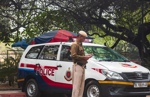 A Delhi police officer stands next to an Indian government vehicle, the Toyota Innova at a check post during the Covid 19 or Corona virus lockdown curfew of entire nation. Delhi, India: A policeman in front of a red and white mini van patrolling the state border of the Delhi, state. singh stock pictures, royalty-free photos & images