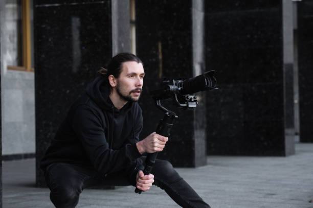 istock Young Professional videographer holding professional camera on 3-axis gimbal stabilizer. Pro equipment helps to make high quality video without shaking. Cameraman wearing black hoodie making a videos. 1216105567