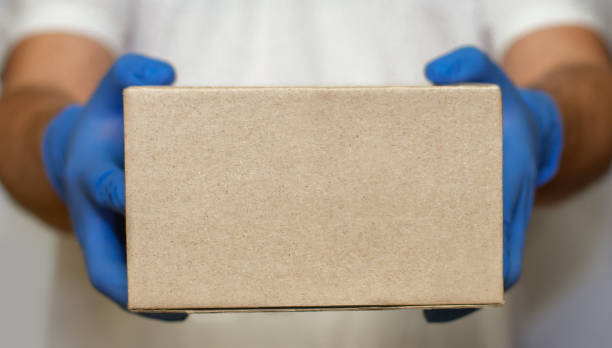 рука в синей медицинской перчатке дает картонную коробку.в знак безопасности почтовых товаров курьерская доставка в карантине вируса или � - sports glove protective glove equipment protection стоковые фото и изображения