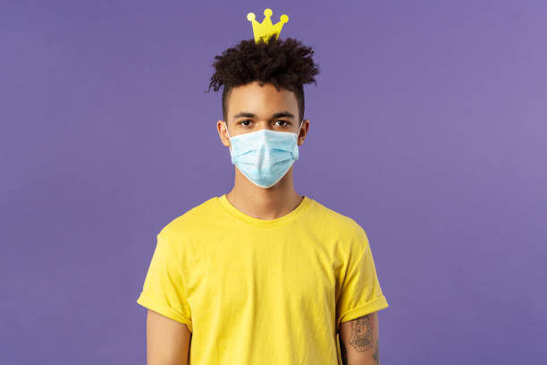 Portrait of funny hispanic guy in face mask, fool around, going crazy staying inside home during quarantine, wearing small crown and look camera, social-distancing, staying healthy covid19 pandemia. retrato de hispano divertido en la máscara de la cara, tonto alrededor, volverse loco quedarse dentro de casa durante la cuarentena, usando una pequeña corona y la cámara de mirada, social-distancing, mantenerse saludable covid19 pandemia