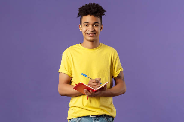 istock Portrait of young hispanic male student studying online courses, writing down lecture, making personal schedule or taking notes in planner, look camera enthusiastic and interested, purple background 1216107067