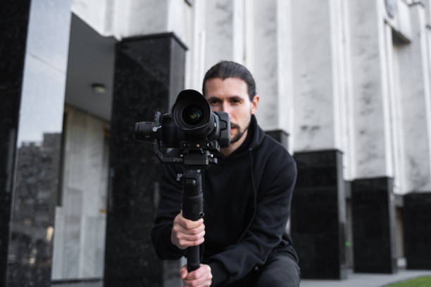 istock Young Professional videographer holding professional camera on 3-axis gimbal stabilizer. Pro equipment helps to make high quality video without shaking. Cameraman wearing black hoodie making a videos. 1216109724