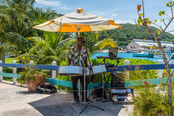 Caribbean musician playing steel drums with the ocean in the background Ocho Rios, Jamaica - April 22, 2019: Local man musician was playing songs on a steel drums near the cruise ship pier in the tropical Caribbean island of Ocho Rios, Jamaica. steel drum stock pictures, royalty-free photos & images