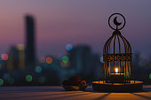 Lantern that have moon symbol on top and small plate of dates fruit with dusk sky and city bokeh light background.