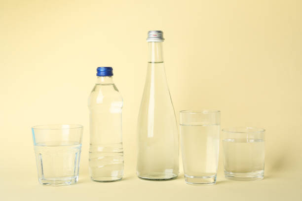 istock Bottles and glasses with water on beige background 1216117791