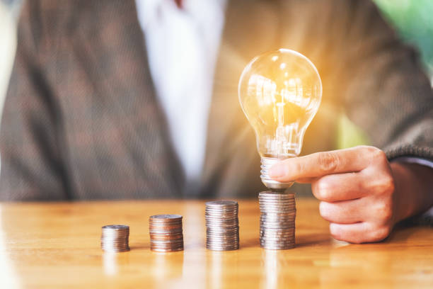 istock Businesswoman holding and putting lightbulb on coins stack on table 1216118045