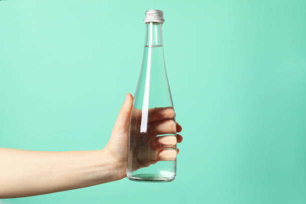 istock Female hand holds bottle with water on mint background, close up 1216120564