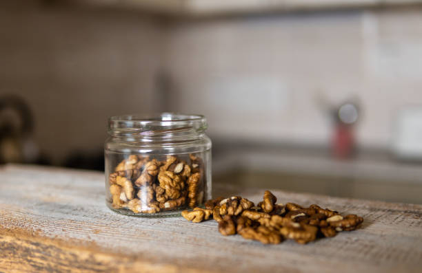 Walnut in a jar and scattered nuts which standing on a white vintage table with a kitchen on background. Walnuts is a healthy vegetarian protein nutritious food. Walnut on rustic old wood