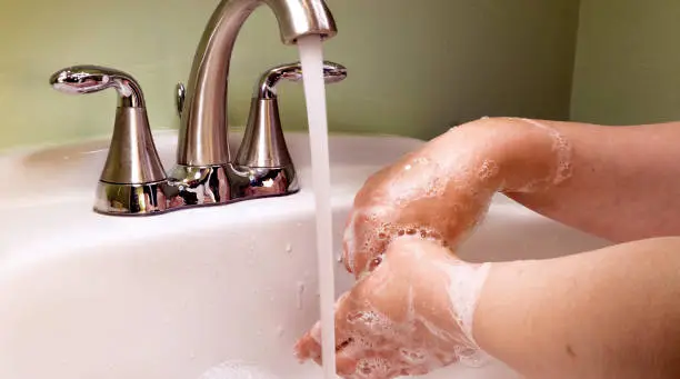 A photo of someone washing their hands with soap and water in a sink