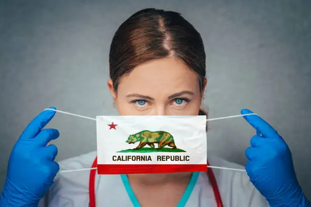 Photo of Coronavirus in U.S. State California, Female Doctor Portrait, protect Face surgical medical mask with California Flag. Illness, Virus Covid-19 in California