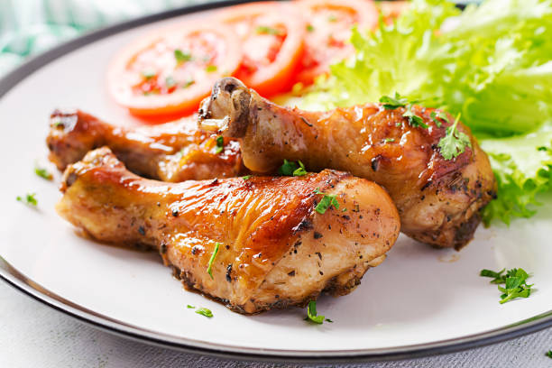 istock Grilled chicken legs with spices and fresh vegetables. Baked drumsticks. 1216128994