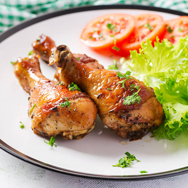 istock Grilled chicken legs with spices and fresh vegetables. Baked drumsticks. 1216129004