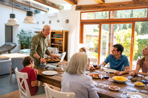 istock Senior Man Holding Paella Pan at Head of Dining Table 1216130020