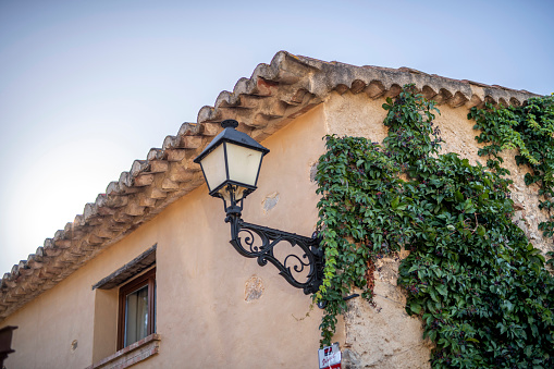 Low angle view of Spanish farmhouse with classic tile roof, wrought iron lantern, and ivy covering one wall.