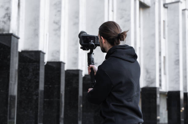 istock Young Professional videographer holding professional camera on 3-axis gimbal stabilizer. Pro equipment helps to make high quality video without shaking. Cameraman wearing black hoodie making a videos. 1216132569