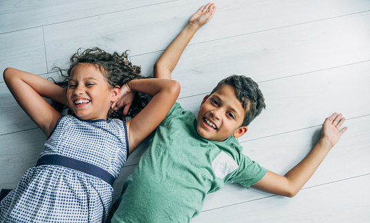 Two smiling mixed race children lying on the floor and smiling.