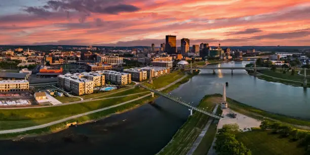 A panoramic aerial drone view over the confluence of the Great Miami and Mad Rivers looking toward downtown Dayton, Ohio under a colorful pink sunset.