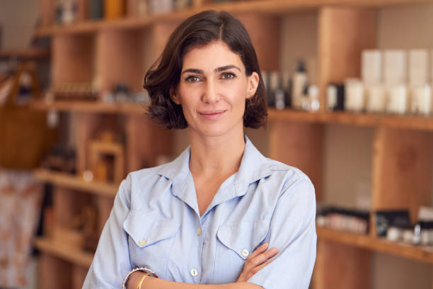 Portrait Of Female Owner Of Gift Store Standing In Front Of Shelves With Cosmetics And Candles Portrait Of Female Owner Of Gift Store Standing In Front Of Shelves With Cosmetics And Candles franchising photos stock pictures, royalty-free photos & images
