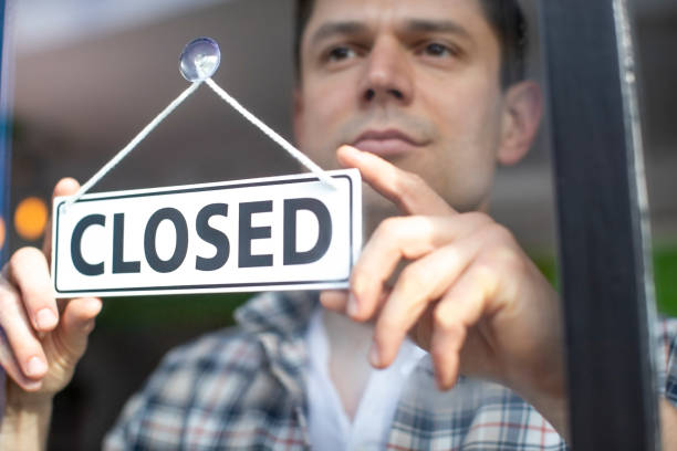 istock Small Business Owner With Serious Expression Putting Up Closed Sign During Recession Or Health Pandemic 1216157288