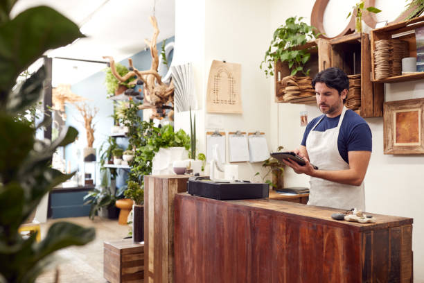 mężczyzna właściciel z cyfrowym tabletem stojący za biurem sprzedaży kwiaciarni - clothing store sales clerk usa clothing zdjęcia i obrazy z banku zdjęć