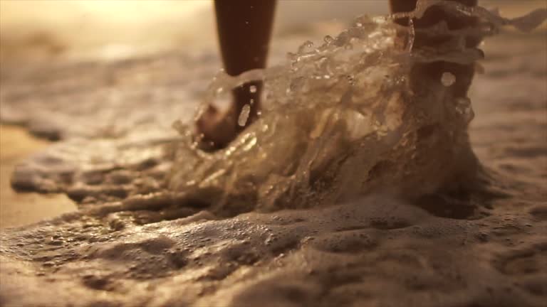 Beautiful scene of a low section of woman walking on ocean beach at sunset